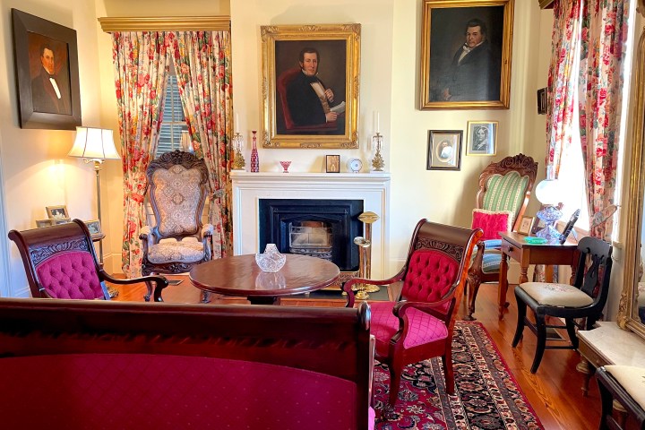 Elegant living room with vintage furniture, floral curtains, and portrait paintings above a fireplace.