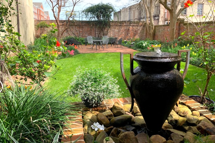 Garden with a pottery fountain, plants, and a seating area on a brick patio.
