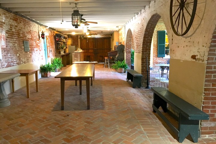 Brick interior with long tables, ceiling fans, plants, and arched openings in a rustic setting.