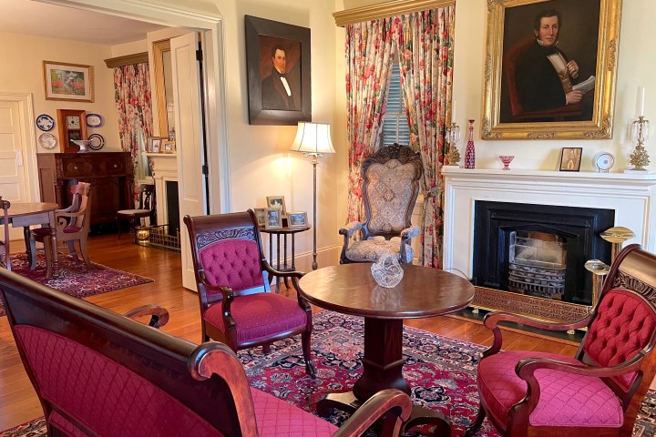 Elegant living room with vintage furniture, red chairs, paintings, fireplace, and floral curtains.