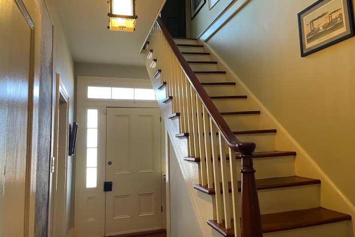 Indoor hallway with stairs, framed pictures, light fixture, and white door with side windows.