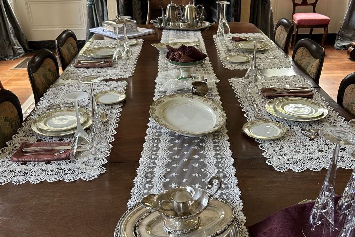 Elegant dining table with lace runner, silverware, and crystal glasses.