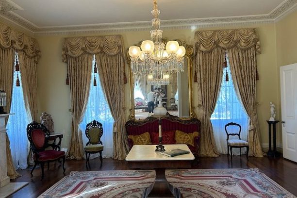 Elegant Victorian living room with plush chairs, chandelier, and ornate curtains.