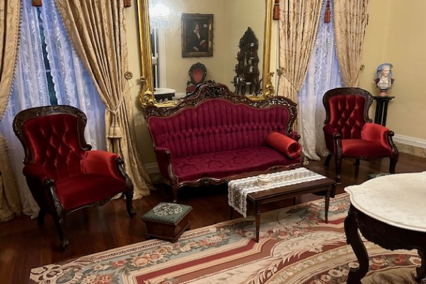 Victorian-style living room with red velvet sofa, armchairs, ornate mirror and patterned rug.