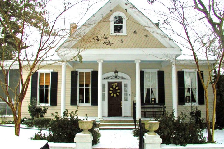 Snow-covered house with columns, dark shutters, and a decorative wreath on the front door.