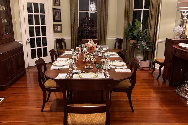 Elegant dining room with chandelier, set table, wooden floors, and large windows.