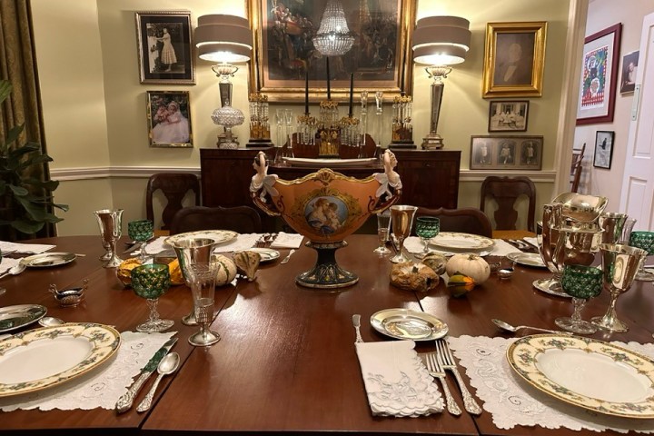 Elegant dining table set with ornate plates, silverware, and decorative centerpiece in a lavish room.