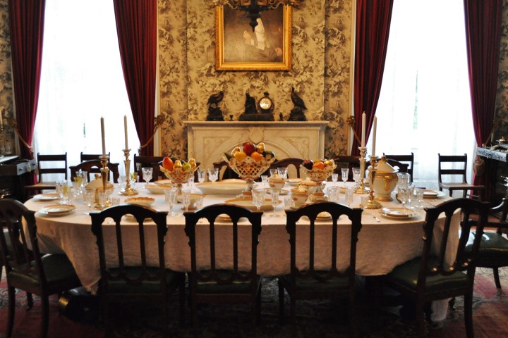 Elegant dining room with set table, chandelier, and red drapes.