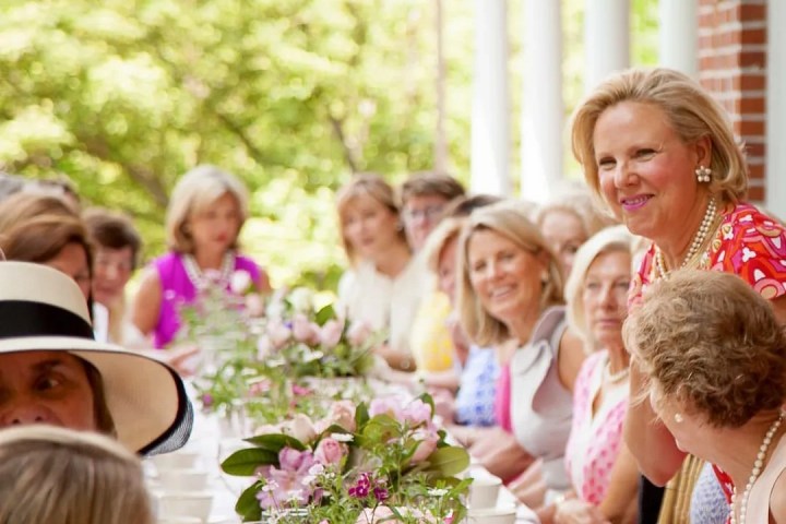 Outdoor luncheon with women seated at a long table adorned with flowers.