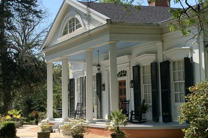 Colonial-style house with white columns, porch, and green lawn.