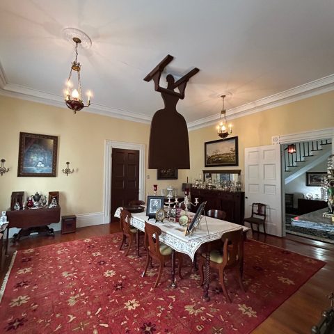 Dining room with large red patterned rug and furniture, silhouette of woman holding a plank on ceiling.