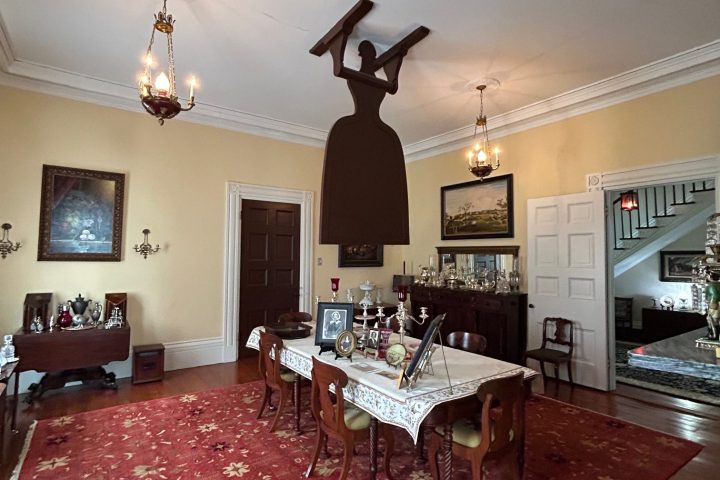 Dining room with large red patterned rug and furniture, silhouette of woman holding a plank on ceiling.