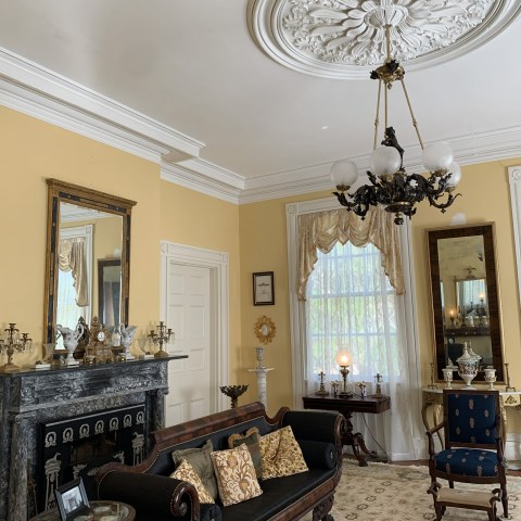 Elegant room with antique furniture, ornate ceiling, and decorative mirror above a fireplace.