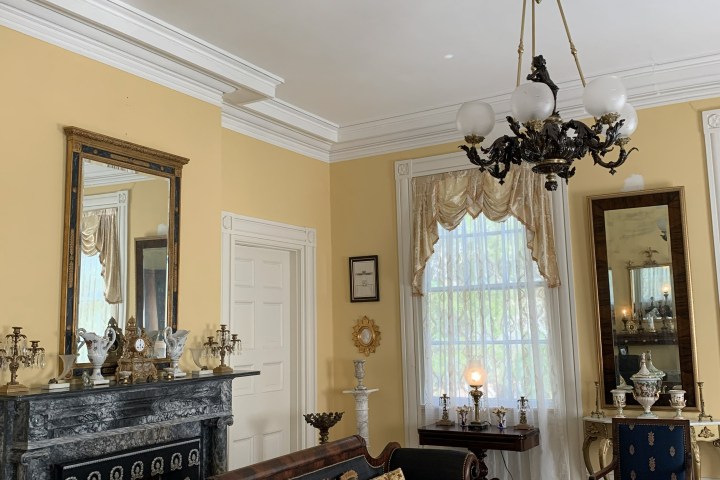 Elegant room with antique furniture, ornate ceiling, and decorative mirror above a fireplace.