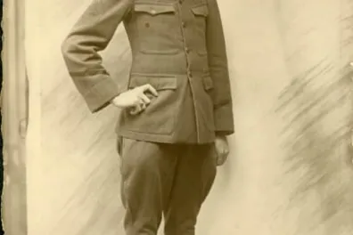 Vintage photo of a man in military uniform with knee-high boots and a cap, posing with hand on hip.