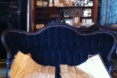 Antique sofa with open maps, bookshelves in background, ornate decor.