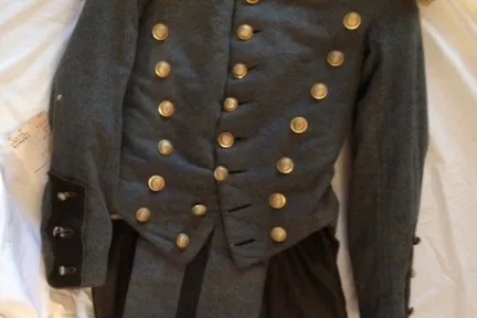 Vintage military jacket with gold buttons and fringed shoulder epaulettes on a white fabric background.