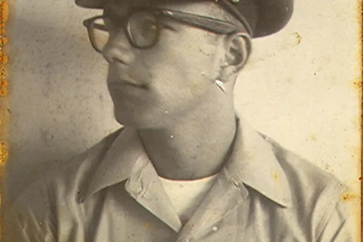 Vintage photo of man in uniform with glasses and cap, looking left.