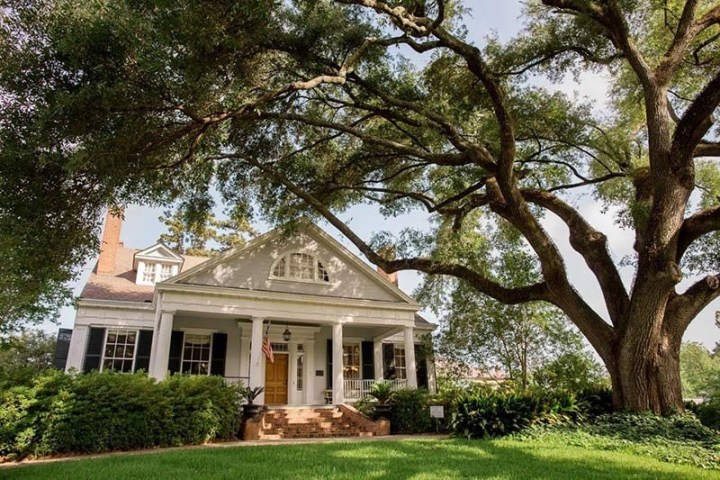 White house with columns, large tree, and lawn in the foreground on a sunny day.