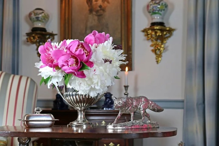 Ornate table with pink and white flowers, silver fox statue, and a painting of a dog in the background.
