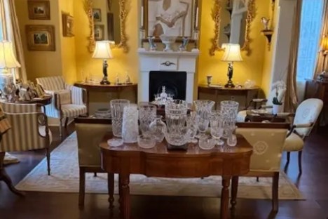 Elegant living room with yellow walls, crystal vases, ornate mirrors, and a chandelier over a wooden floor.