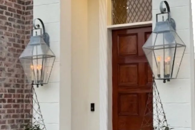 Elegant wooden door with two lanterns and potted plants on either side.