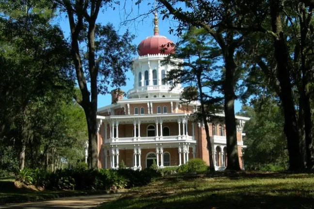 Historic brick mansion with white columns and red dome amidst trees.