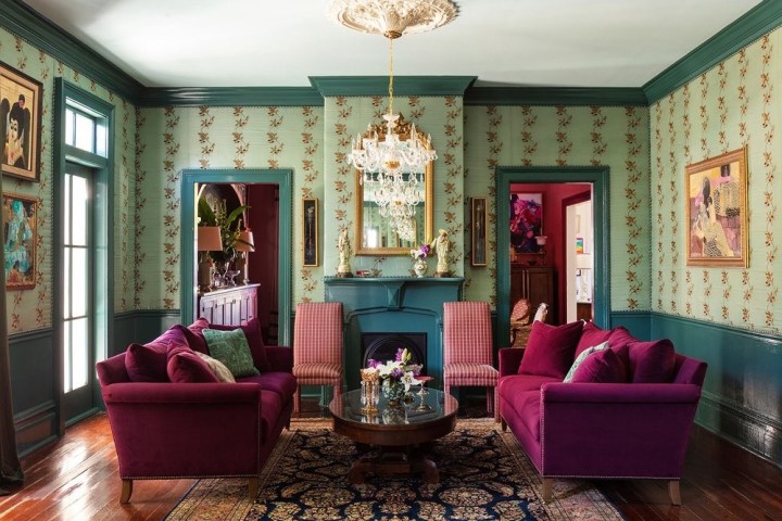 Elegant living room with purple sofas, ornate wallpaper, chandelier, and large mirror above fireplace.