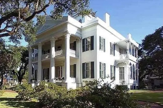 Elegant white mansion with columns and green shutters surrounded by trees.